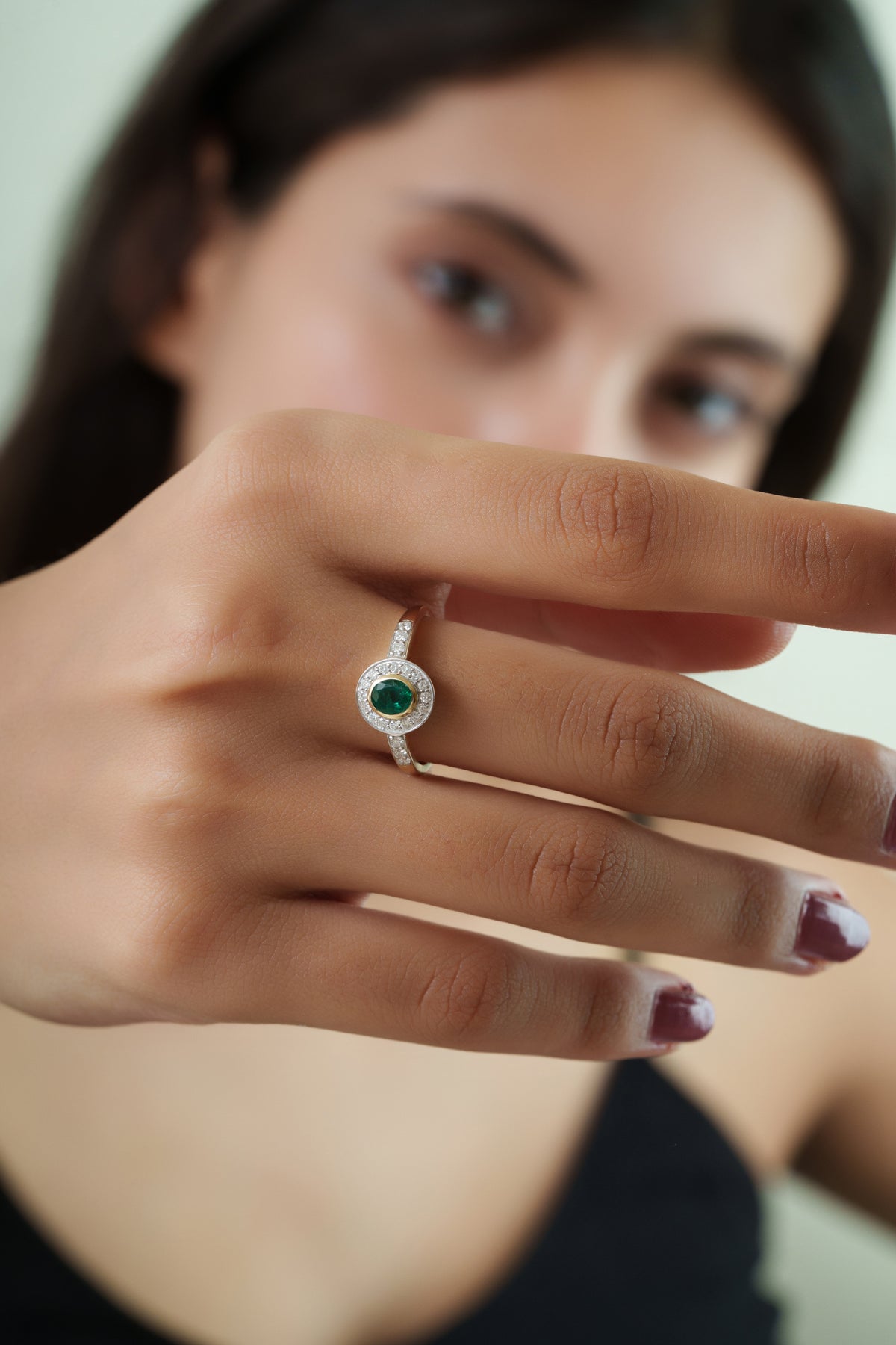 Elegant 14K yellow gold ring featuring a natural oval emerald surrounded by a brilliant diamond halo with diamond-accented shoulders in a timeless vintage-inspired design.
