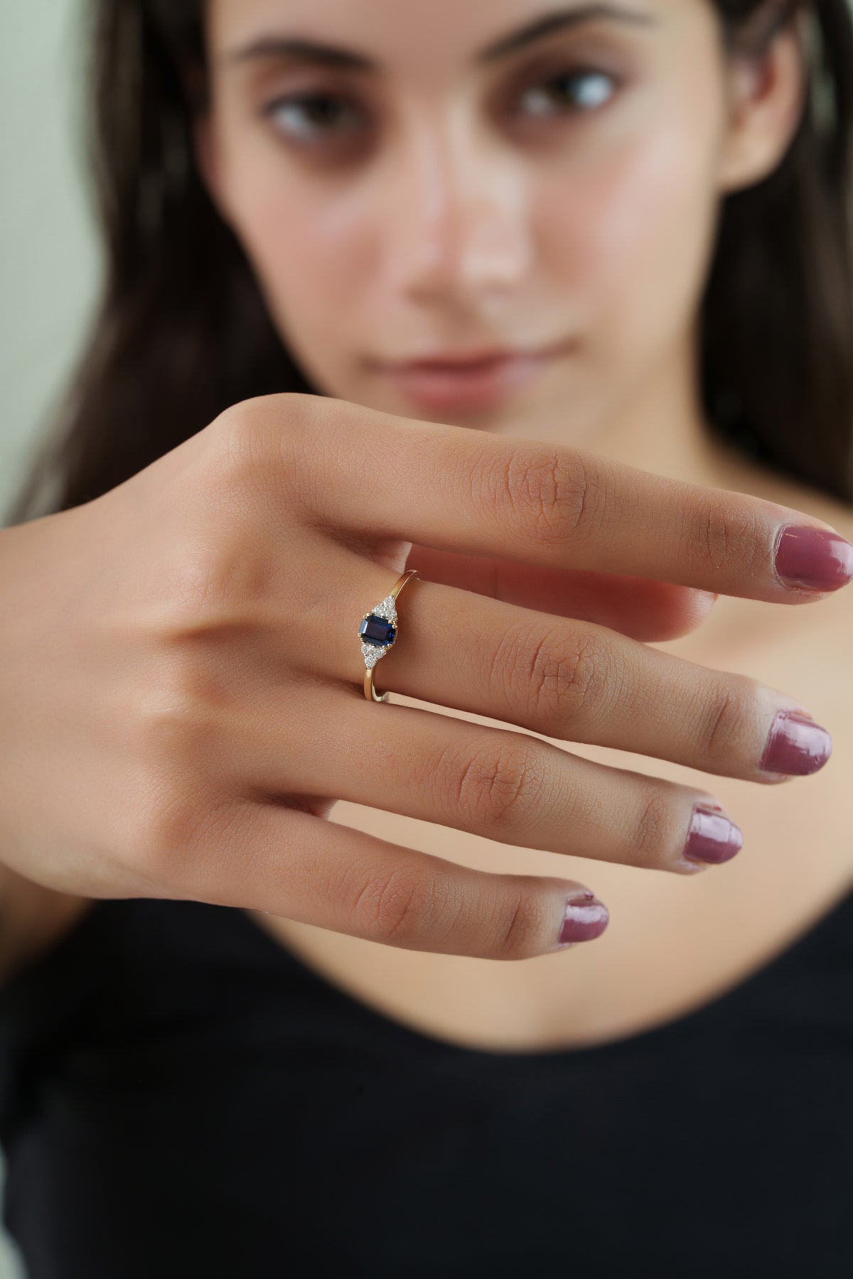 Elegant gold ring featuring a natural emerald-cut blue sapphire with sparkling round diamond side clusters, handcrafted as a timeless engagement, anniversary, or September birthstone ring for women.