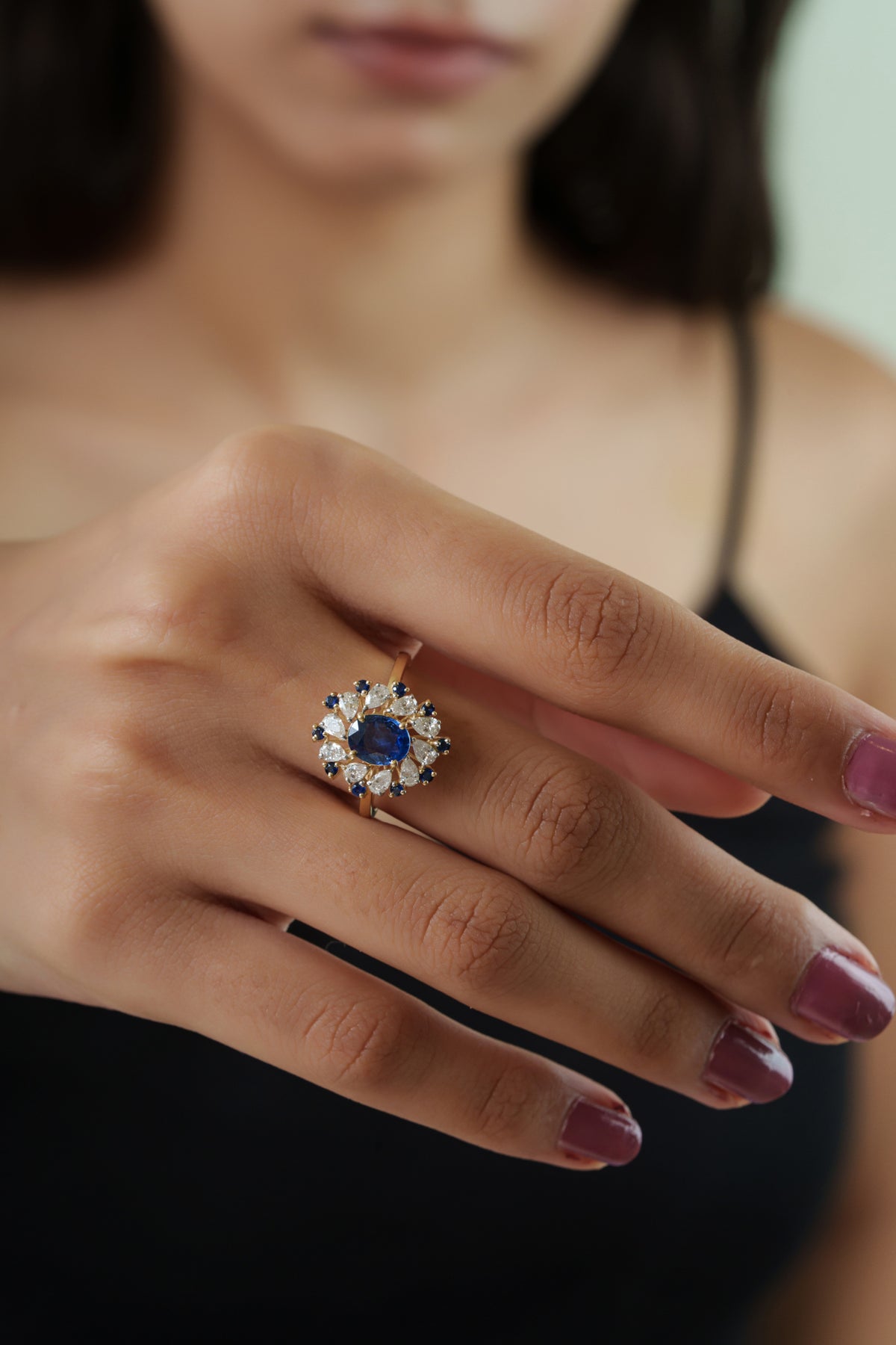 Luxury 14K yellow gold ring featuring an oval natural blue sapphire surrounded by pear-cut diamonds and round blue sapphire accents in a floral halo design.